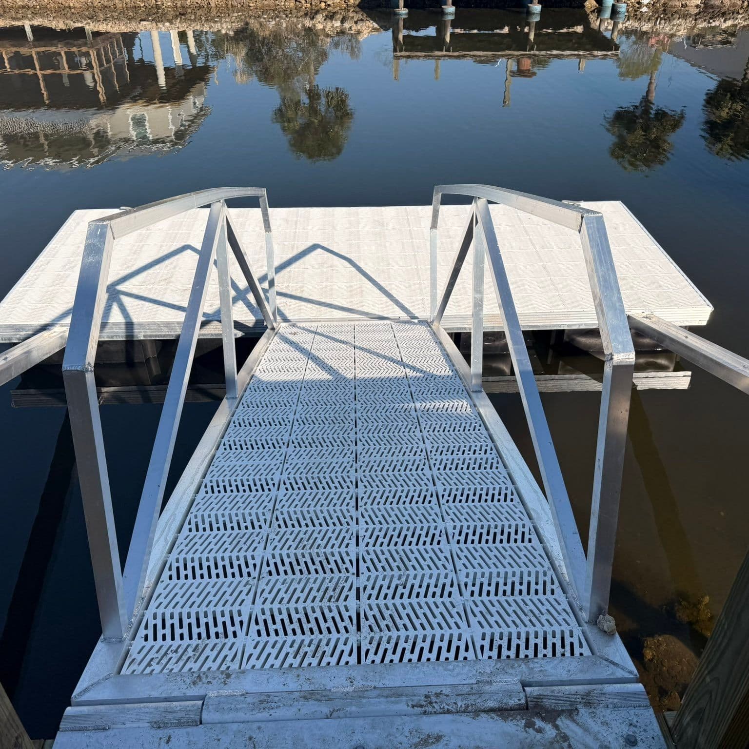 Aluminum gangway with curved handrails leading down to a floating dock with grated decking