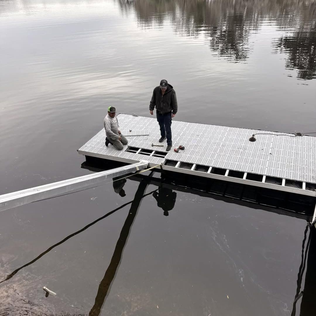 Two crew members working on a floating dock section out on the water