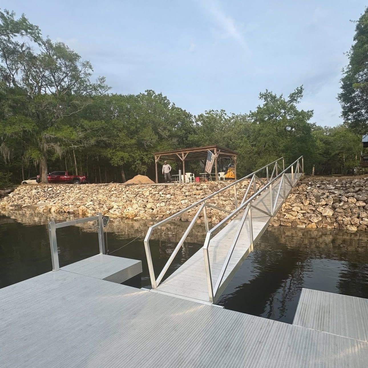 Floating dock and aluminum gangway below a rock riprap shoreline with a pergola on the bank