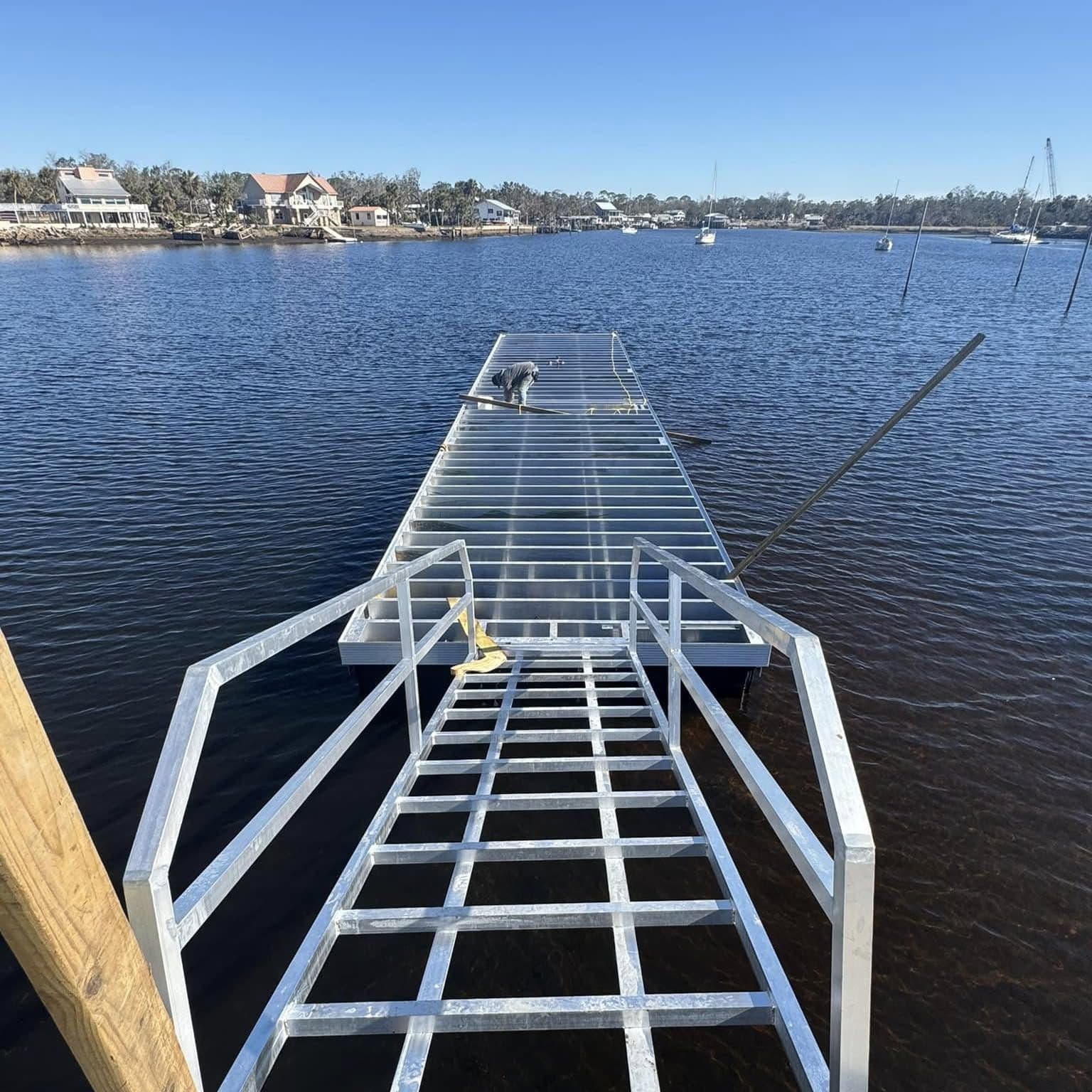 Aluminum gangway leading out to a floating dock on wide open water with homes on the far shore