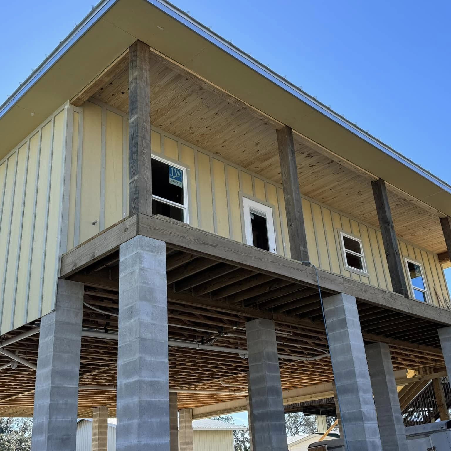New two-story home with pale yellow siding set on tall concrete-block piers, floor framing visible from below