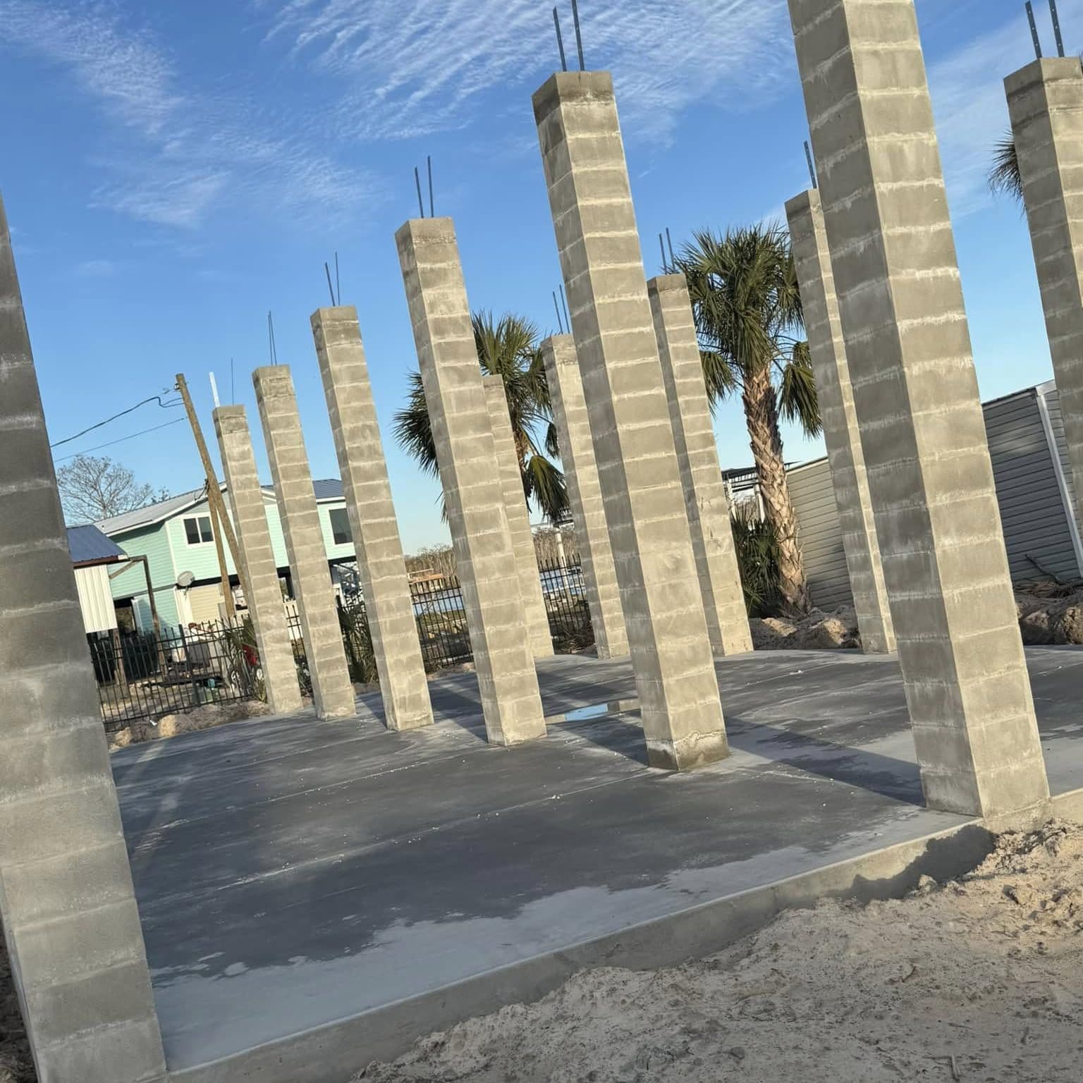 Row of tall concrete-block pier columns with rebar sticking out the tops, standing on a new concrete slab