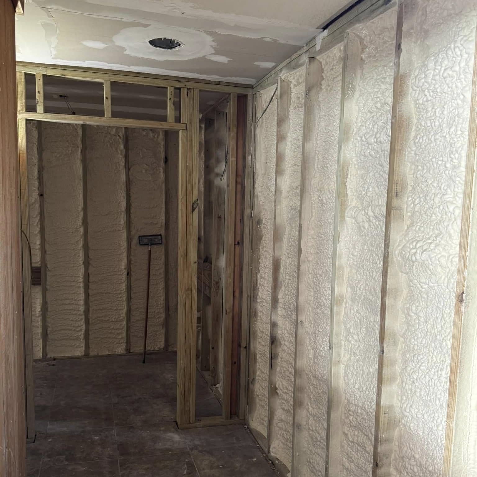 New wood-framed doorway and walls with fresh spray-foam insulation, ceiling patched around a recessed light opening