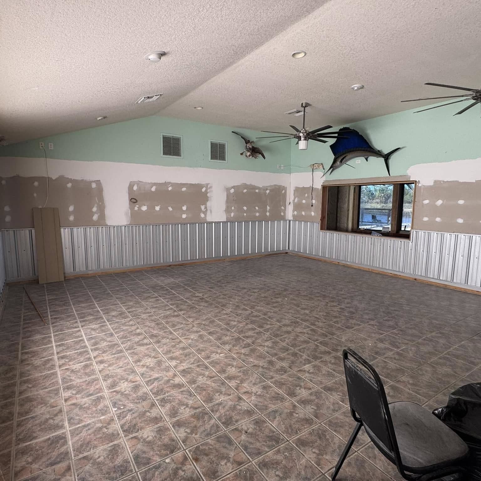 Large open room mid-remodel with a tile floor, patched walls, ceiling fans and mounted fish on the wall