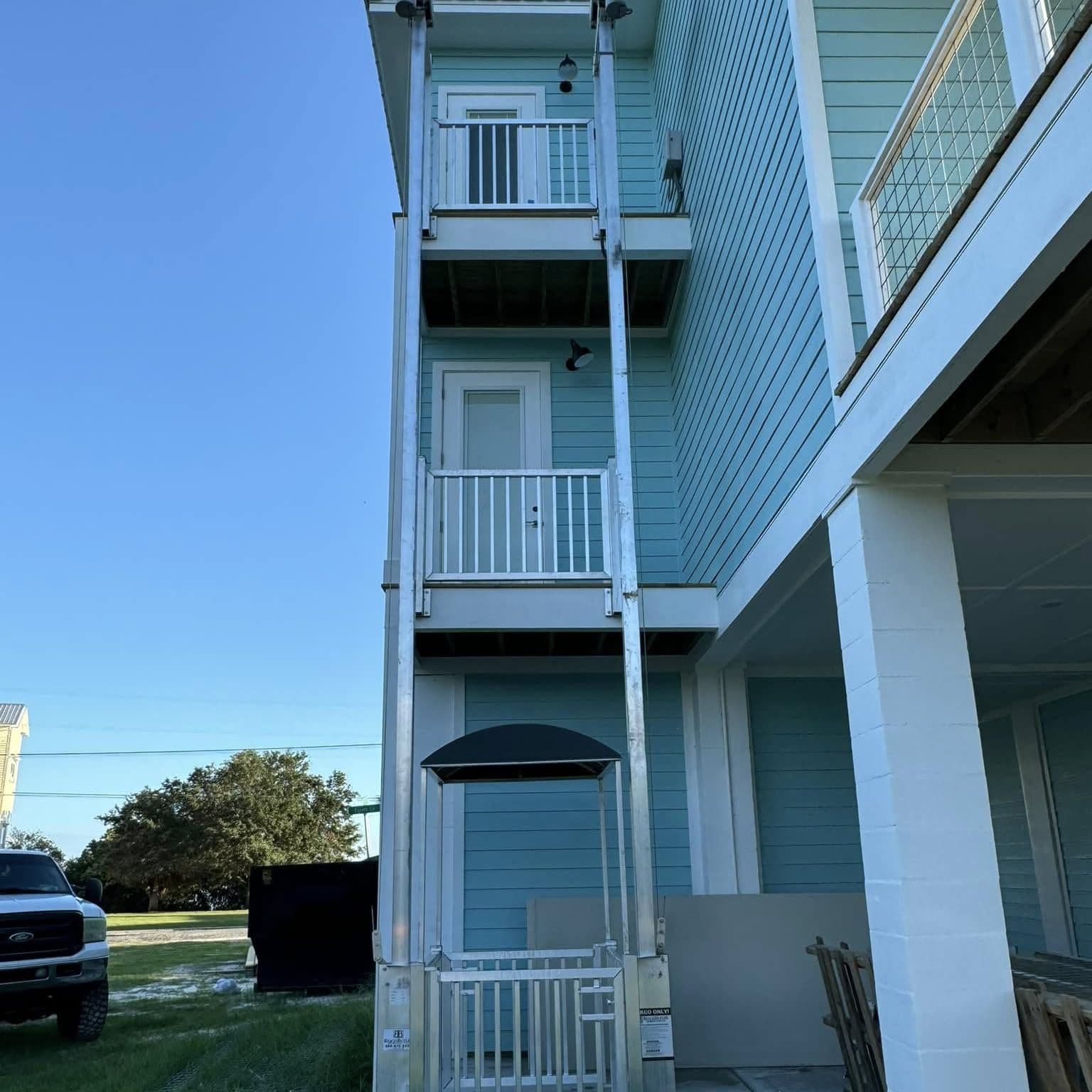 Aluminum cargo lift tower running up three stories on a light blue raised home, canopy-topped lift car at ground level