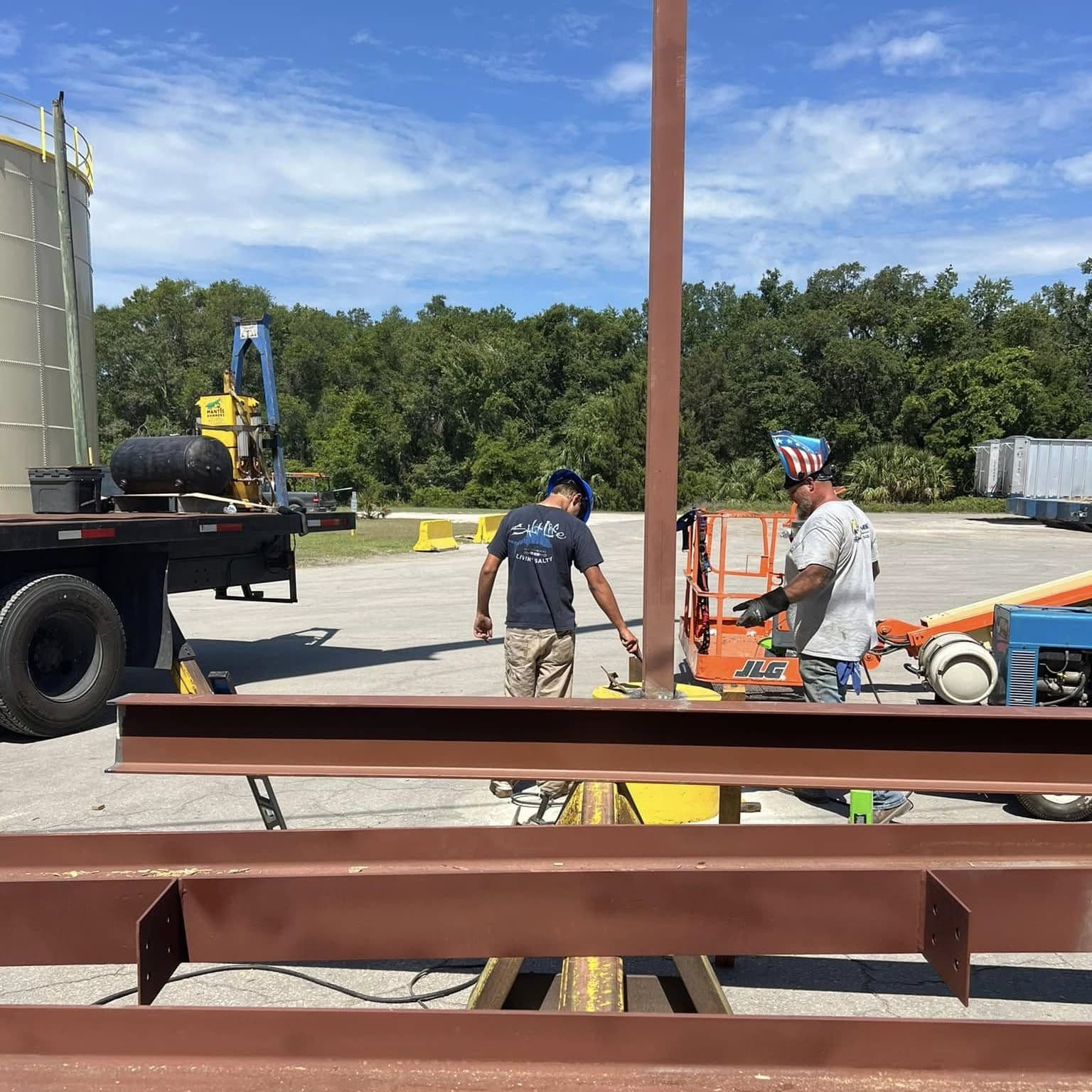 Crew members working on red-primed steel columns on site, with a truck and lift behind them