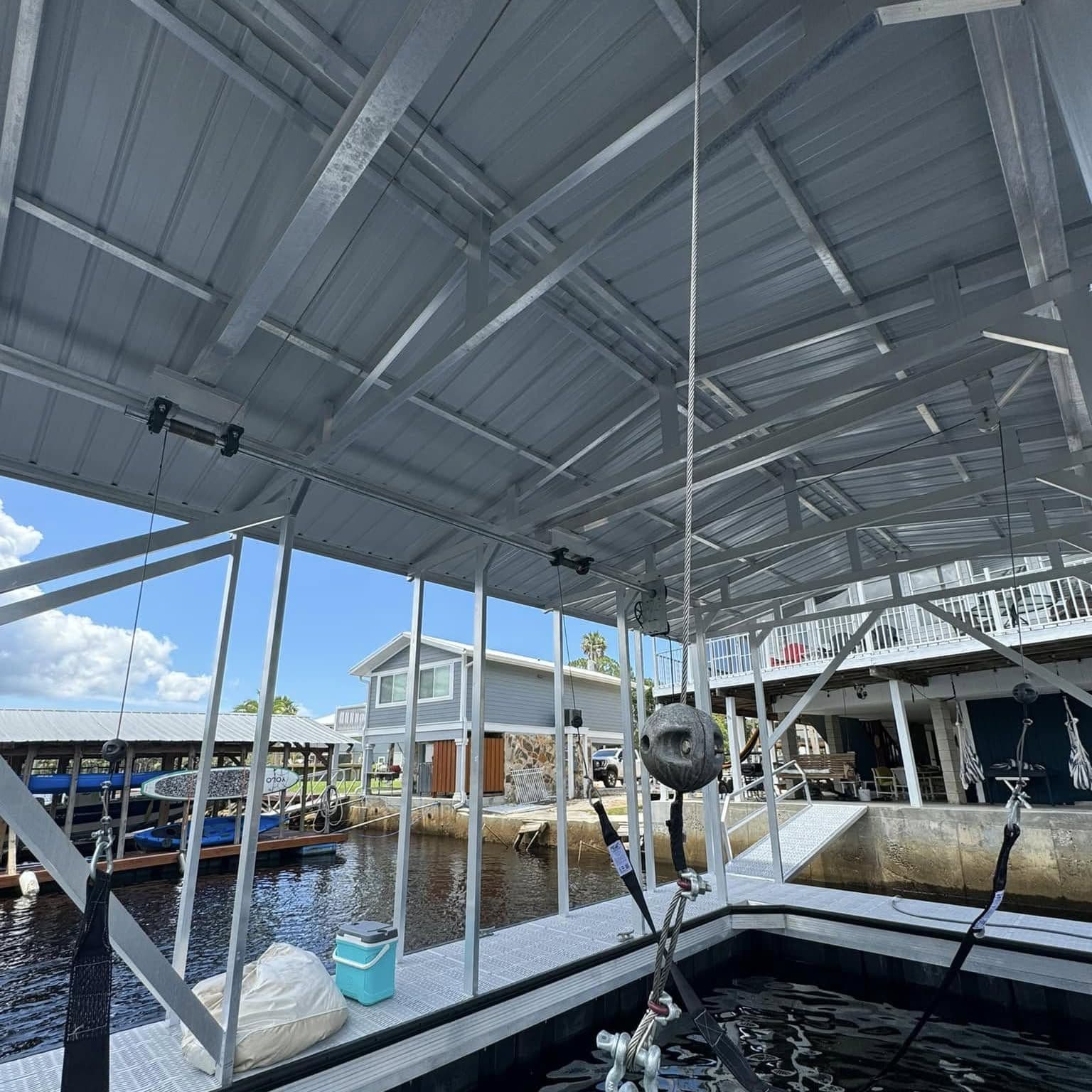 Boat lift cables and slings hanging under the aluminum canopy of a floating boat slip