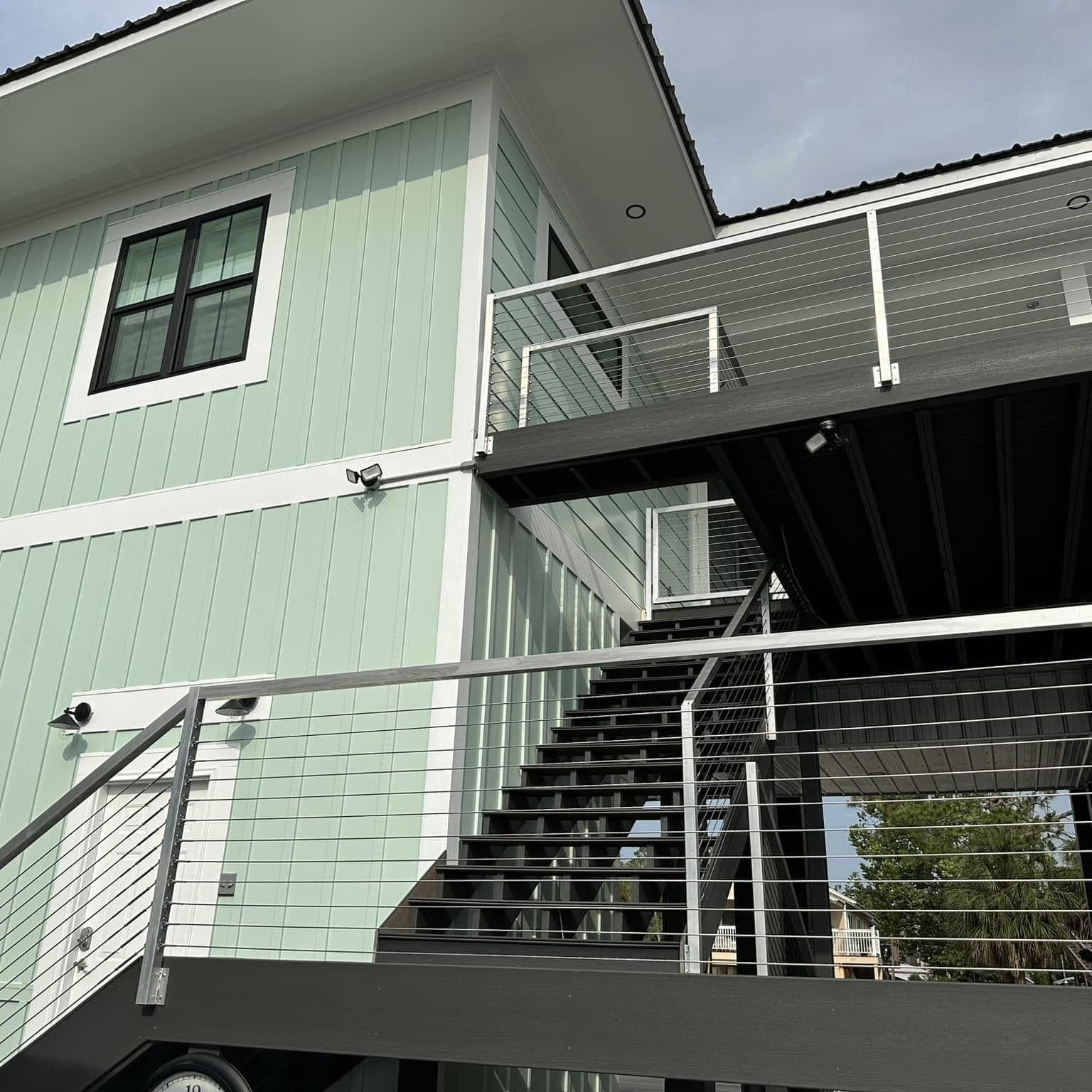 Dark stairway with stainless cable railing climbing to the upper deck of a mint-green raised home