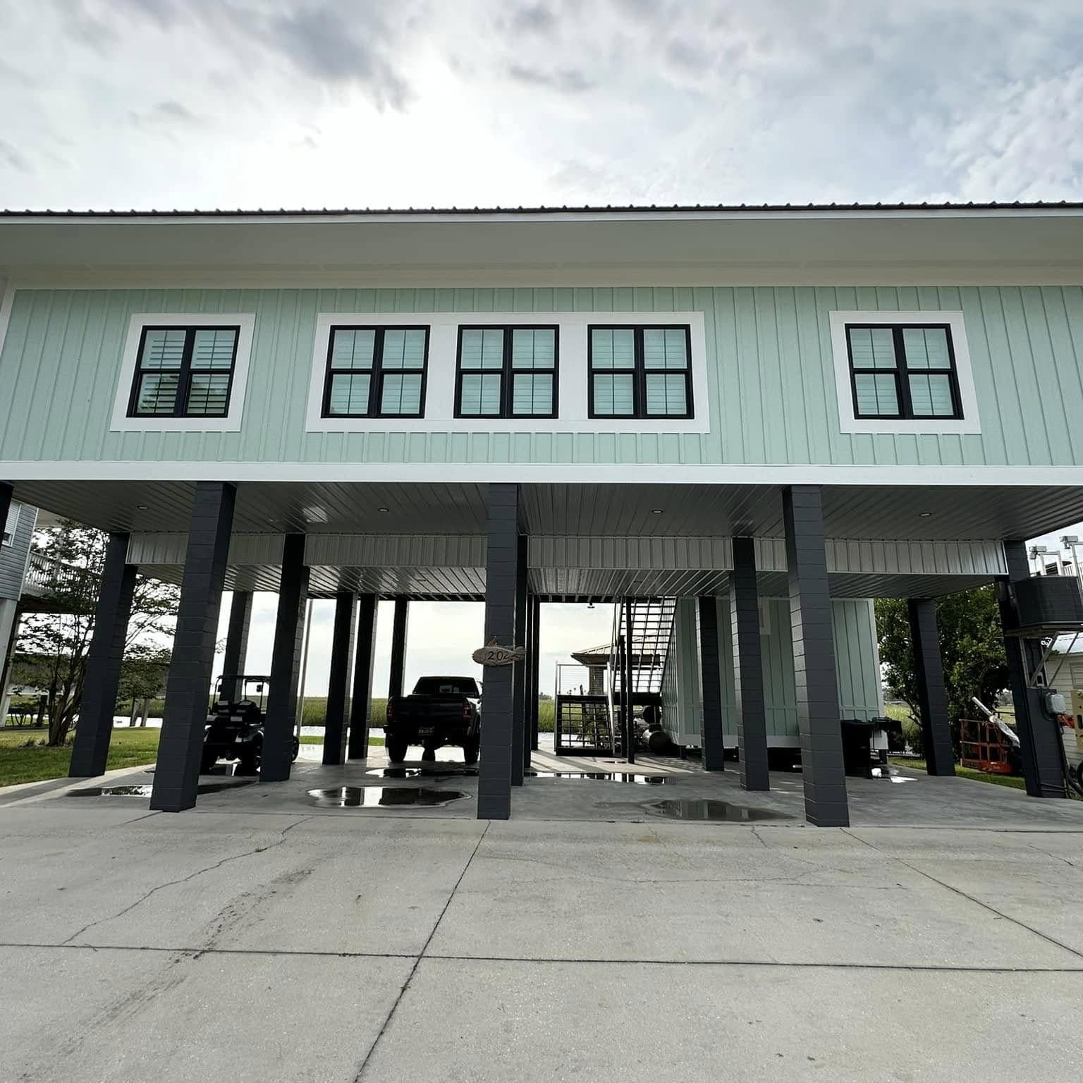 Finished mint-green raised home on dark columns with a row of black-framed windows and vehicles parked on the slab underneath