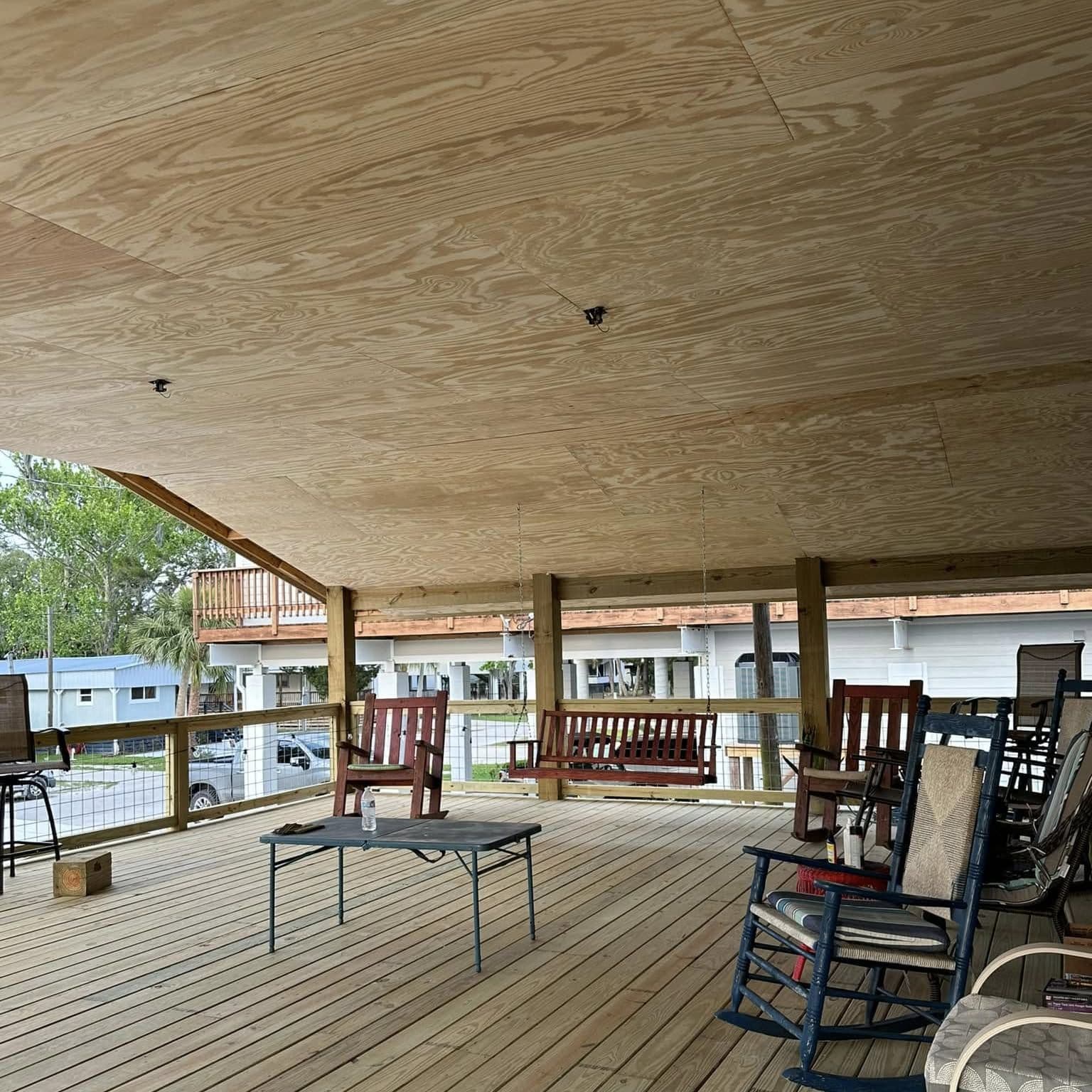 Large covered wood porch with a plywood ceiling, rocking chairs and a porch swing