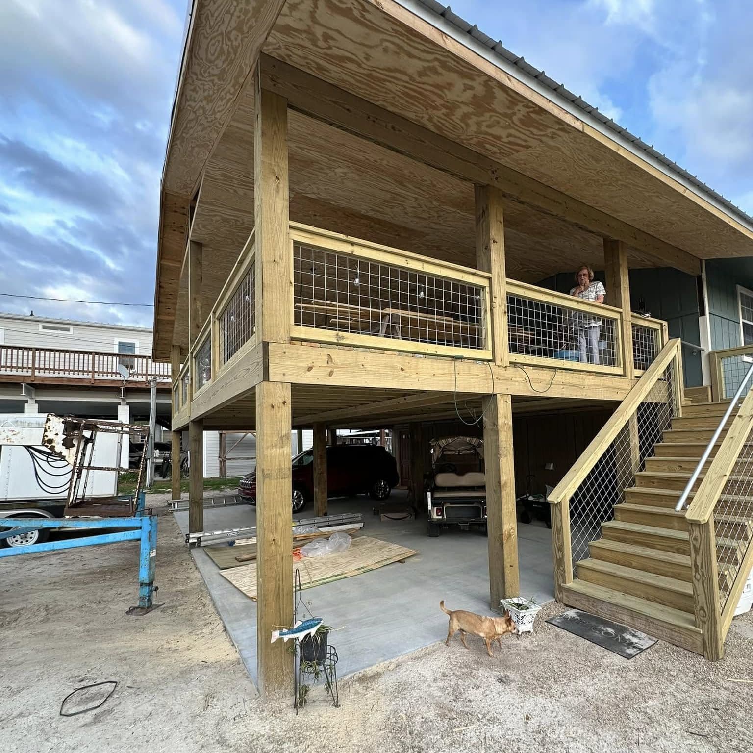 Raised wood-frame home with a covered porch, wire-panel railings and wide wood stairs down to a sandy lot