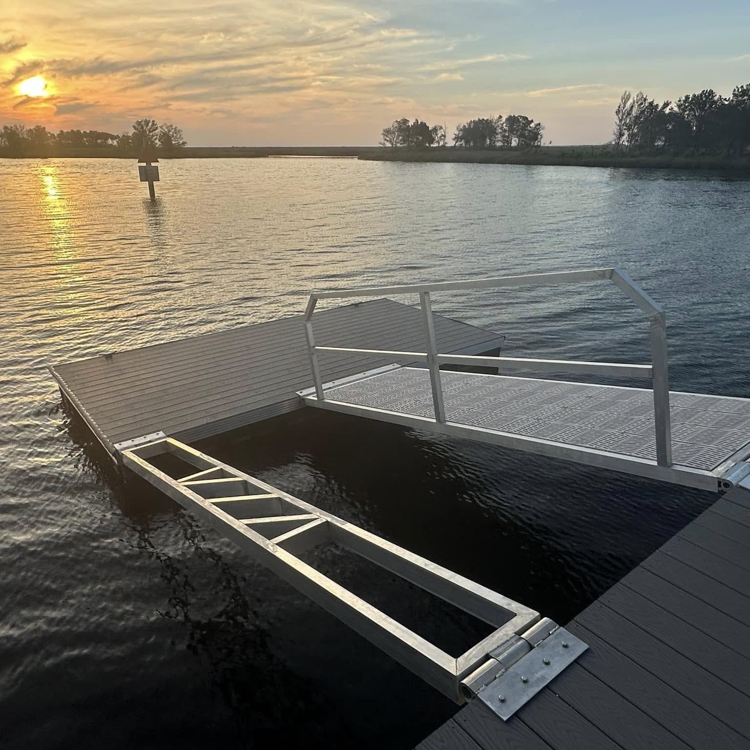 Floating dock with aluminum railing and gangway frame at sunset on open water