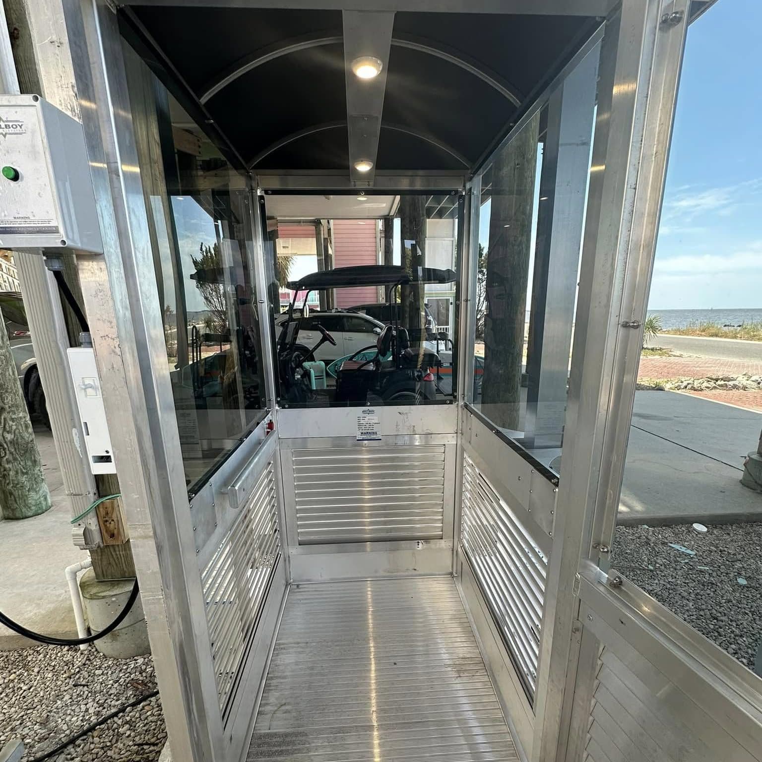 Inside an enclosed aluminum lift cab with glass sides and a lit ceiling