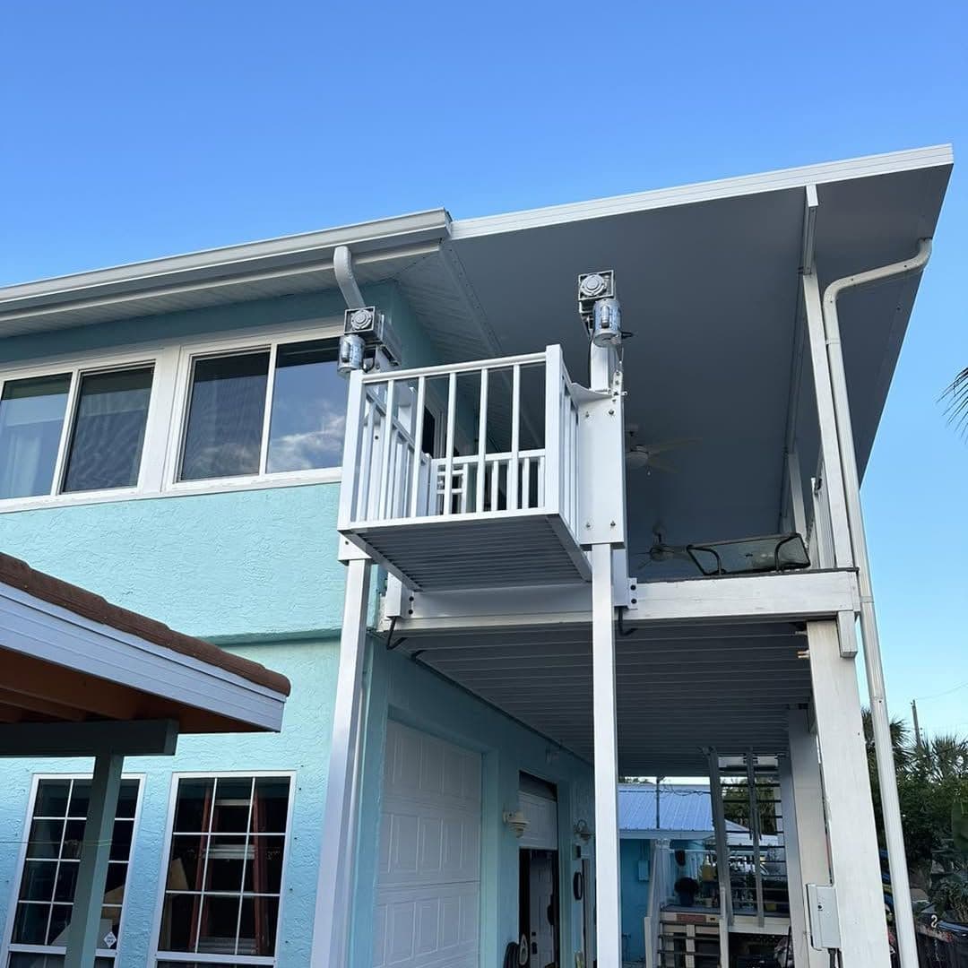 Cargo lift car with white railings at the top landing on the side of a light blue two-story home