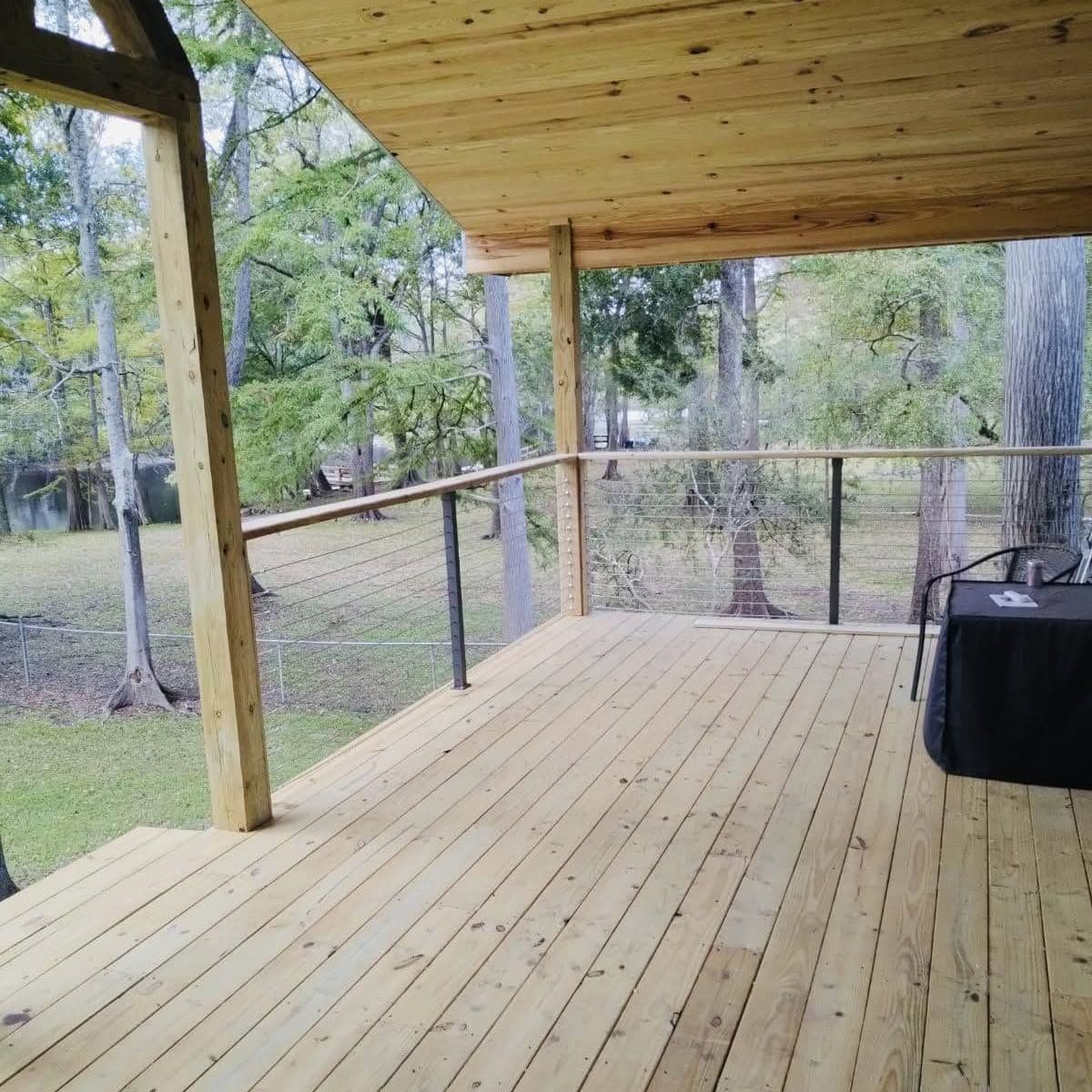 New covered wood deck with cable railing overlooking a wooded yard