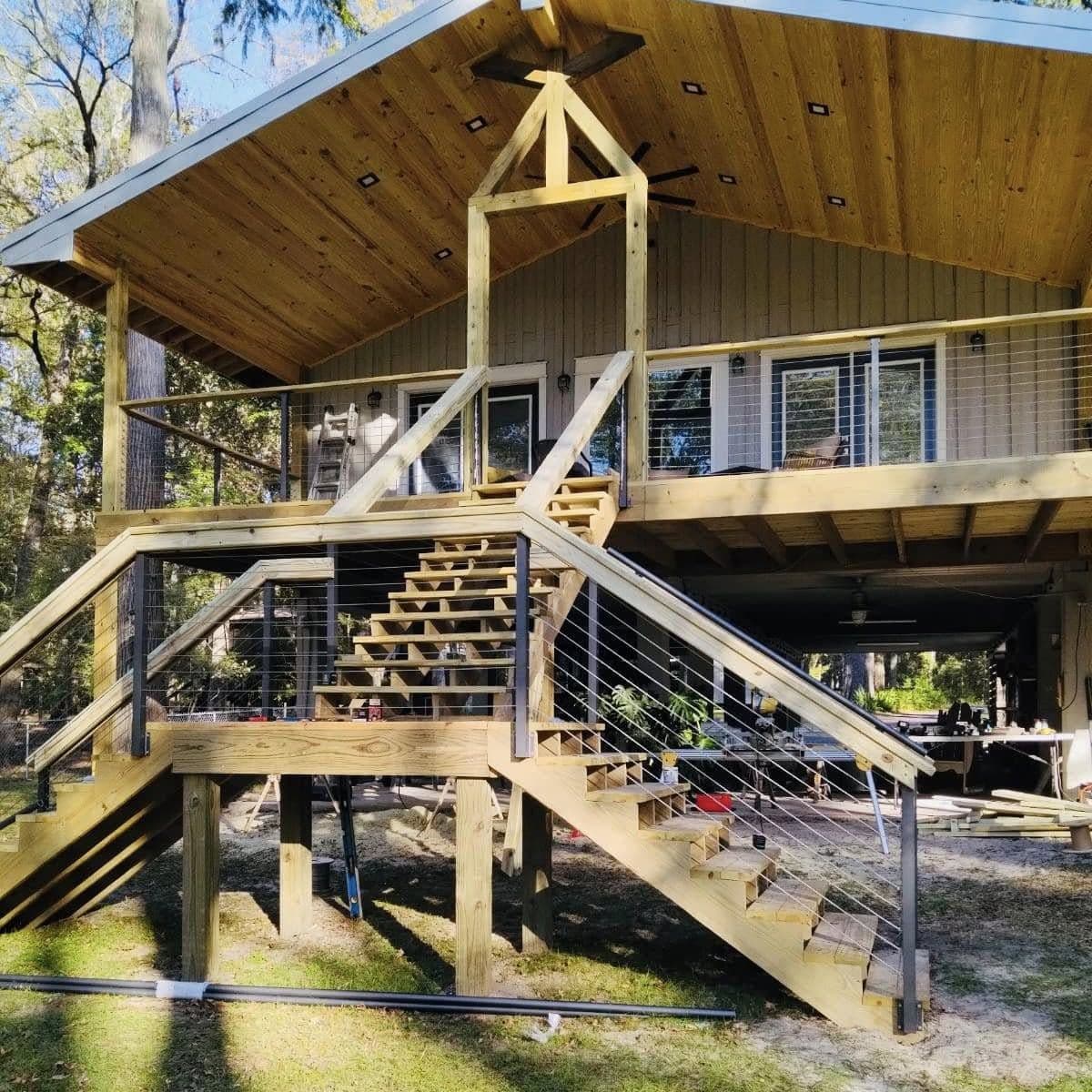 Raised home with a tall tongue-and-groove gable porch, ceiling fan and wide wood stairs with cable railing