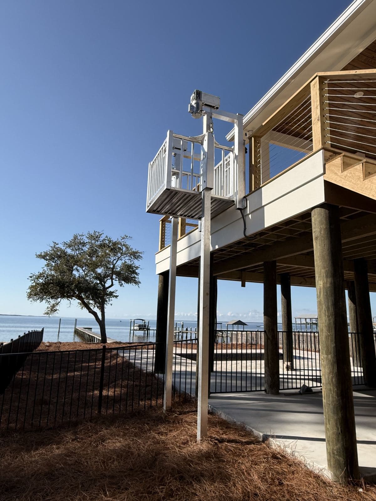 Cargo lift tower beside a waterfront raised home with the lift car at the upper deck