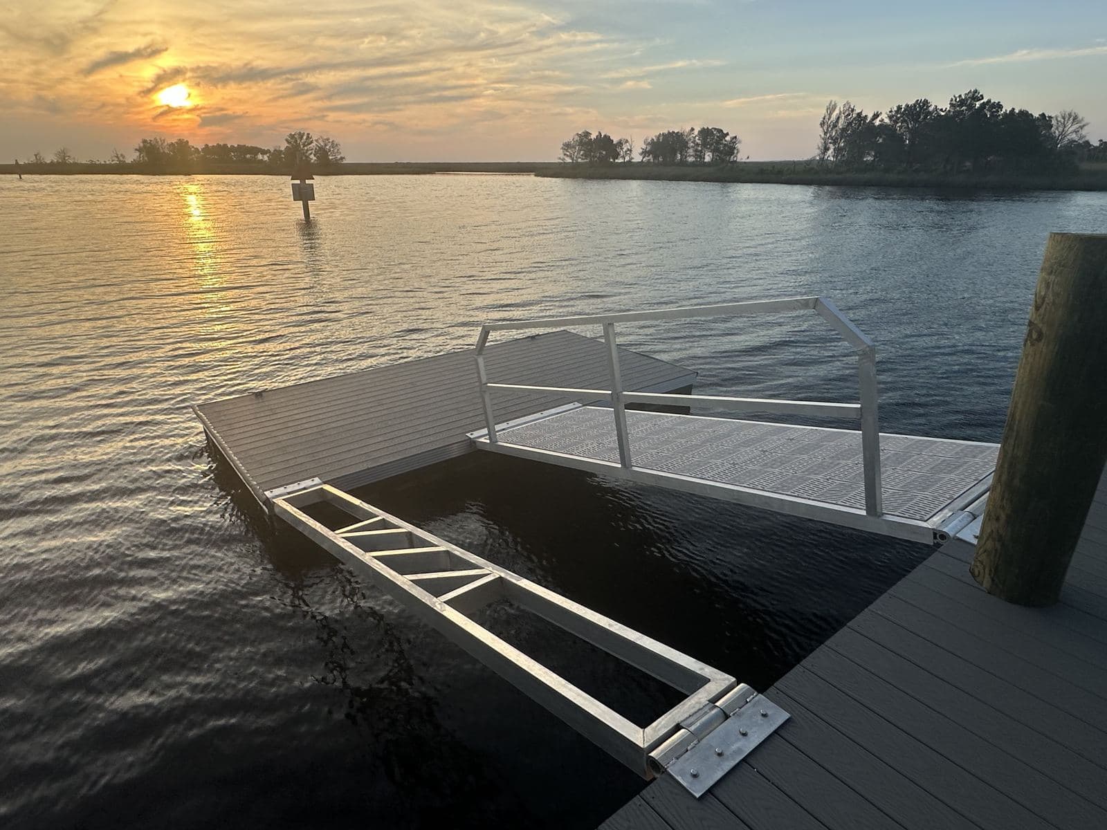 Floating dock with an aluminum frame and railing on open water at sunset